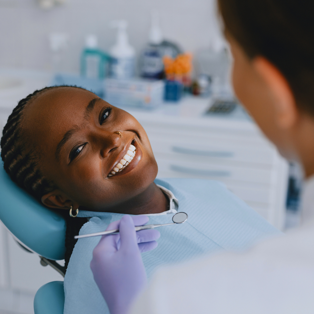 Woman smiling in a dental chair while a dental professional prepares to bond a tooth gem